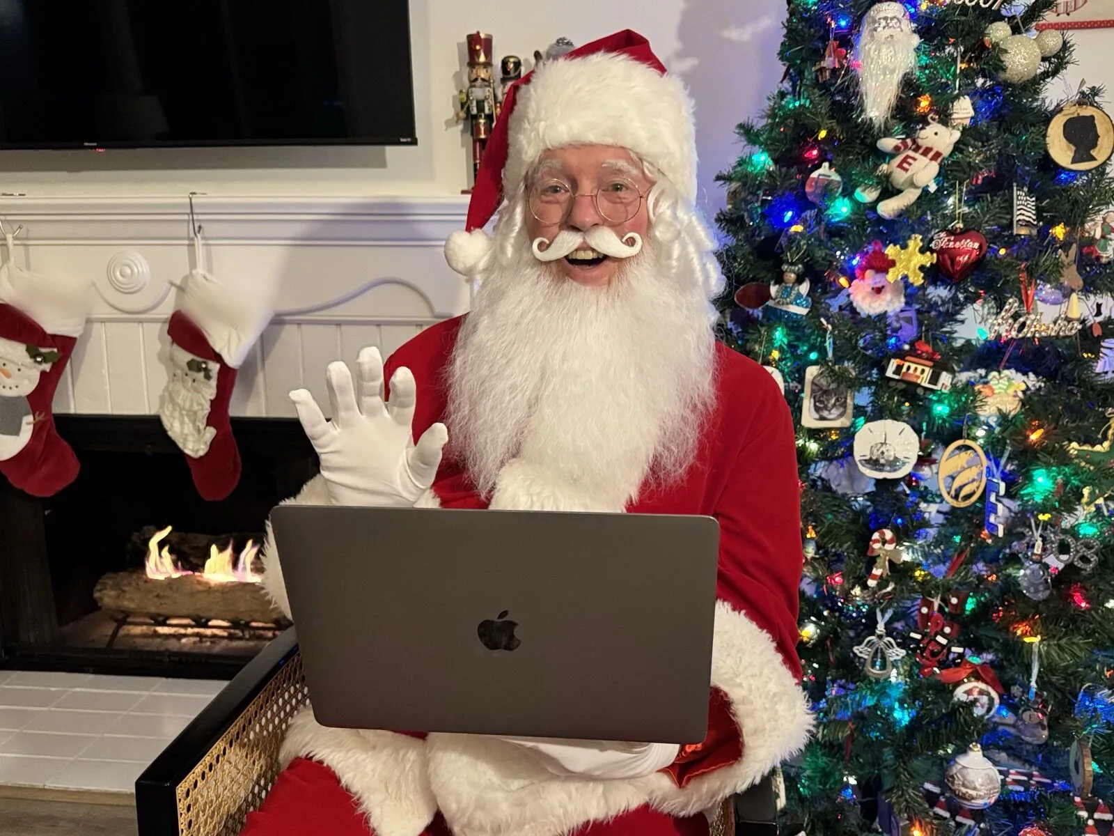 Santa on a laptop screen during a live video call, seated in a room with a fireplace and a decorated tree